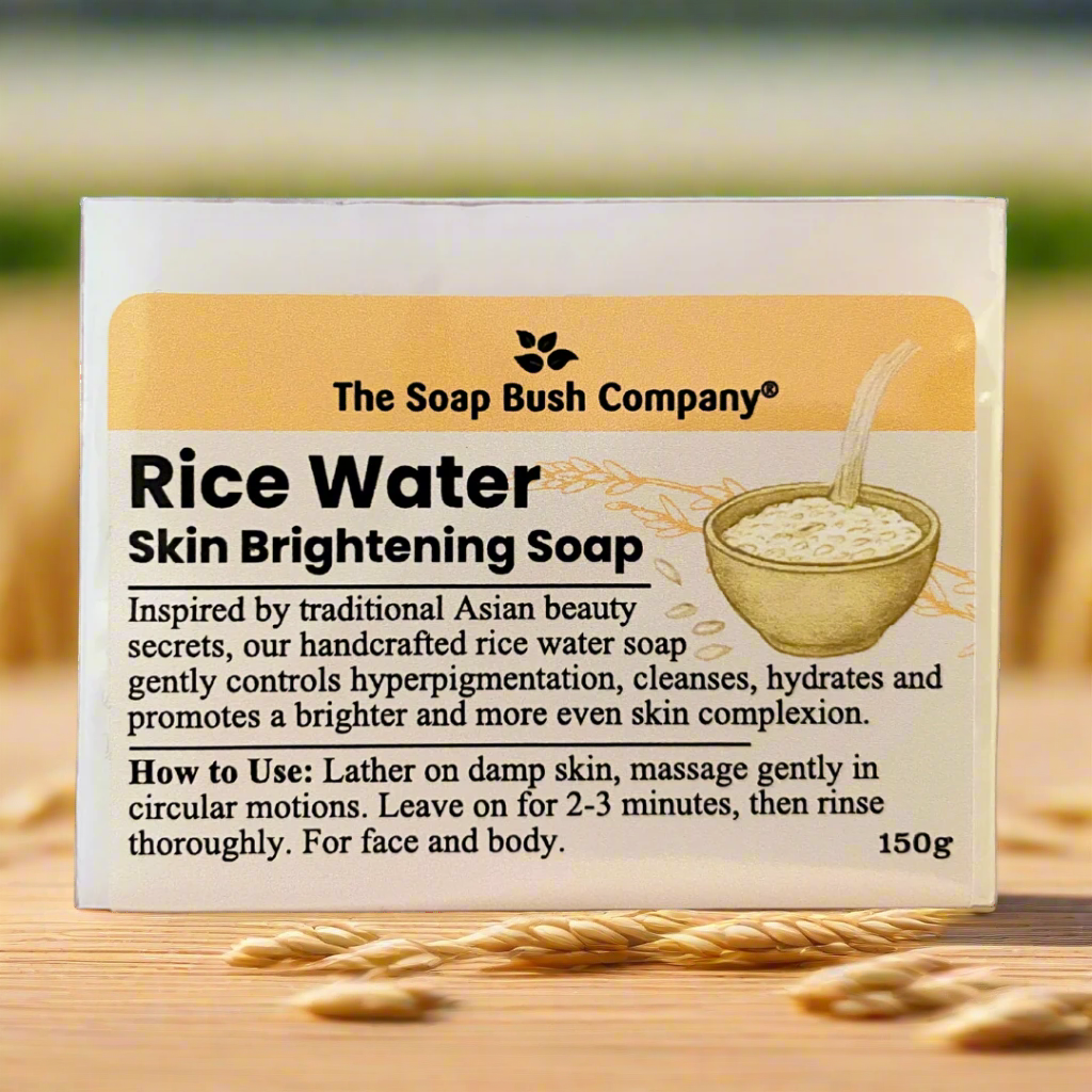 Soap packaging for Rice Water Skin Brightening Soap by The Soap Bush Company on a wooden surface with rice grains. the sopa bush company rice waster skin brightening soap